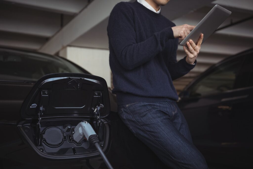 man using digital tablet while charging electric car