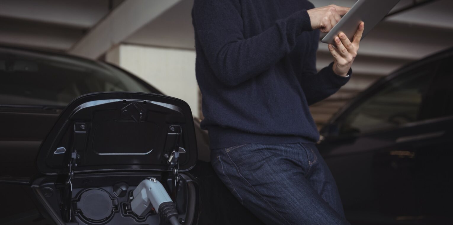 man using digital tablet while charging electric car